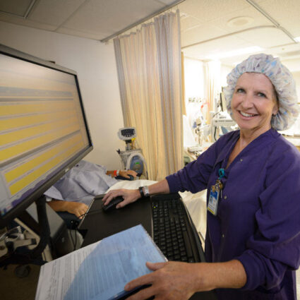 Nurse enters patient information on computer at patient bedside.