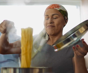 Woman wearing scarf checking cooking spaghetti for doneness.