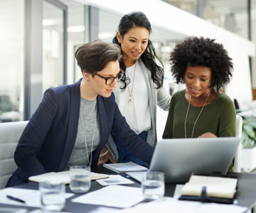 Three office workers gathered together looking at a lap top screen and talking.