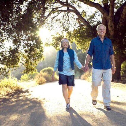 Couple holding hands and walking on a path surrounded by trees.