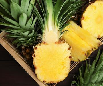 Tasty cut pineapples in crate on wooden table, flat lay