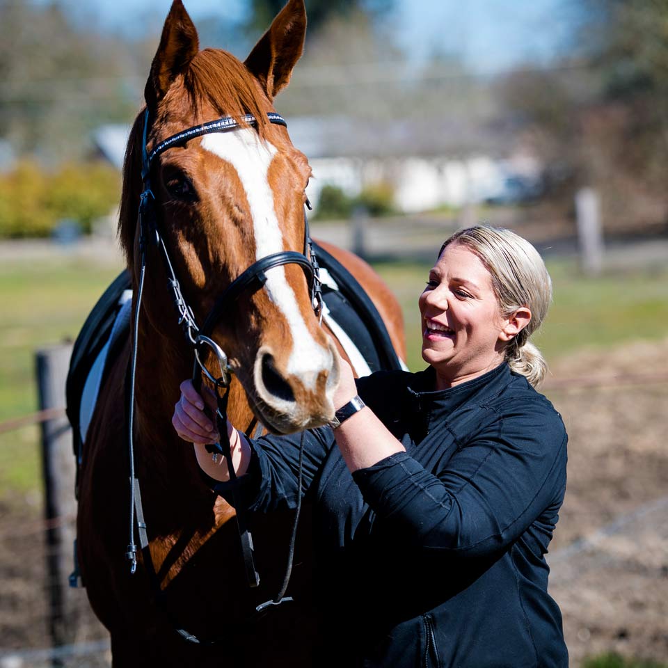 Close up of Amie smiling as she pats her horse.