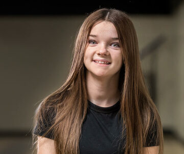 Sweet home girl Ava smiles as she sits in her school's gymnasium.