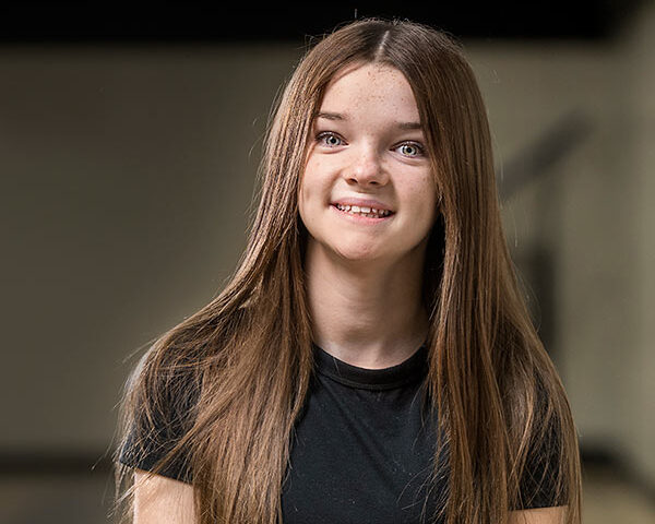 Sweet home girl Ava smiles as she sits in her school's gymnasium.