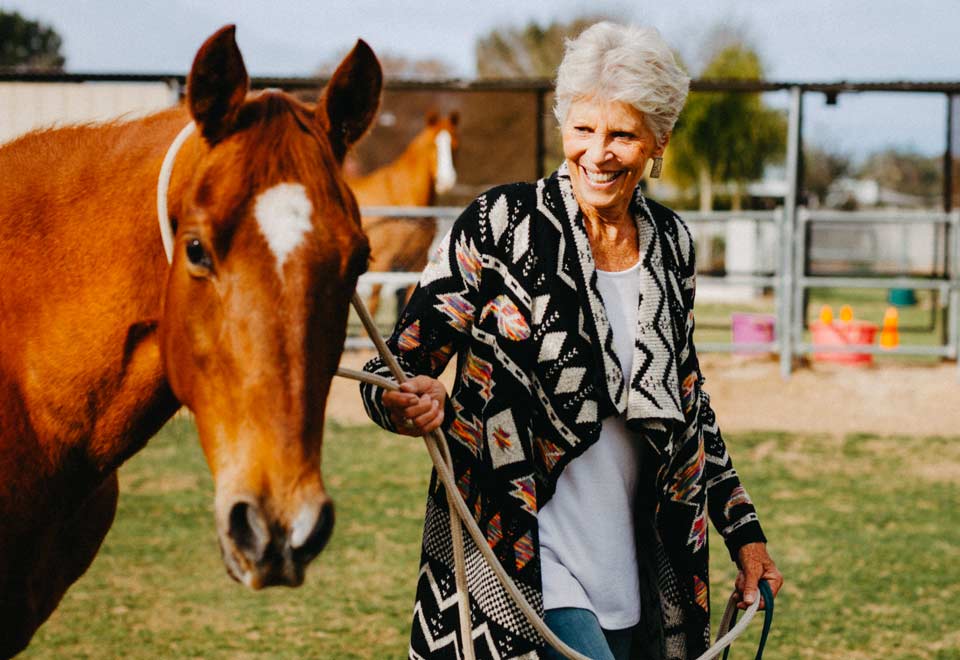 A smiling Kathy leading a horse by its bridle.