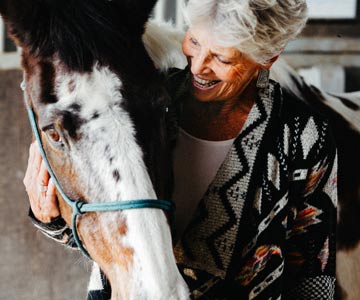 A close up of Kathy smiling as she holds the head of a painted horse close to her.