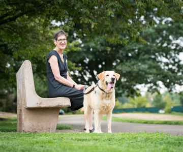 Marilyn sitting on a park bench with her dog beside her.