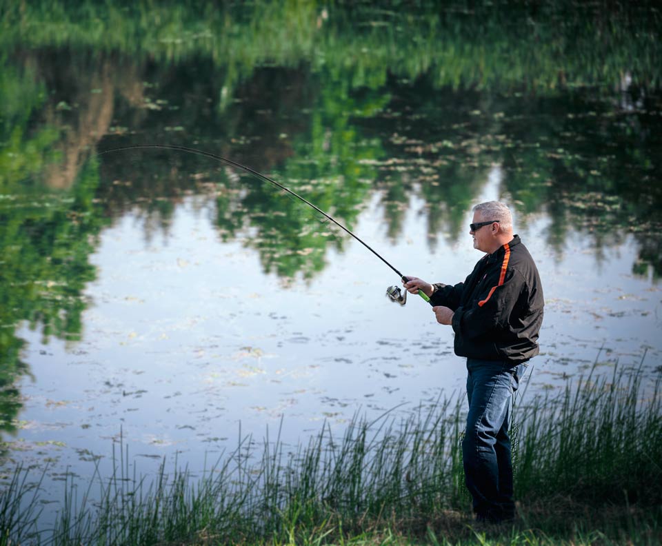 Matt outdoors in front of a small lake fishing.