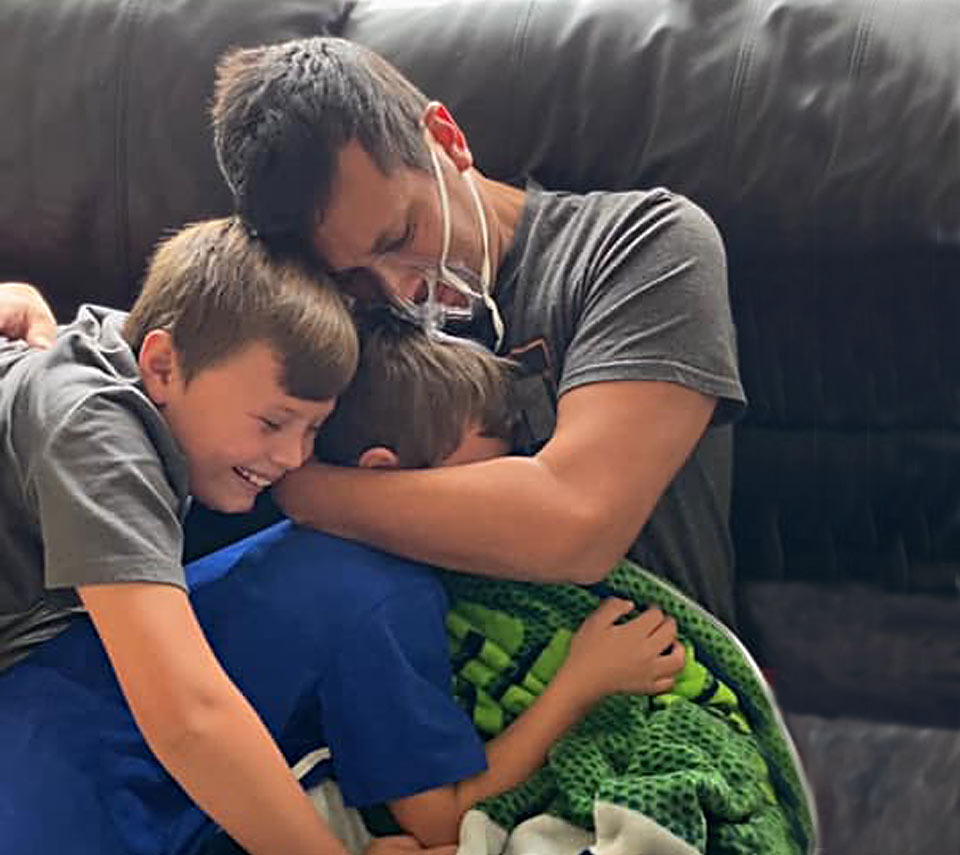 Mike in a mask holding his two boys close after coming home from the hospital.