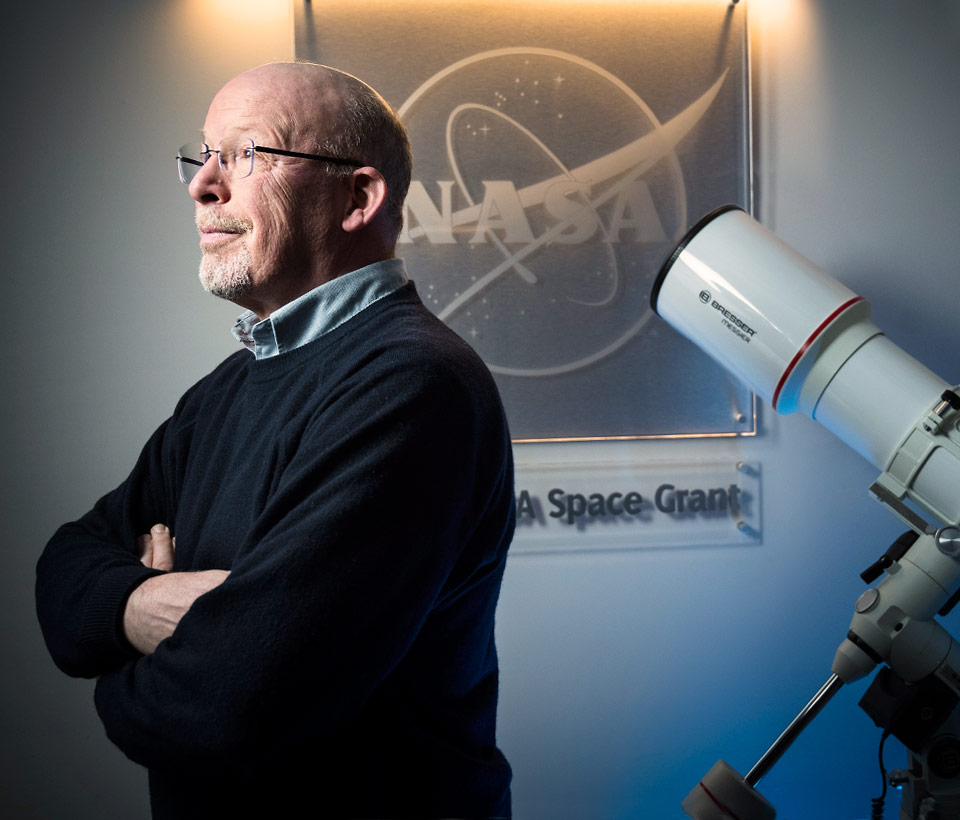 Randall with arms crossed with a NASA picture behind him.