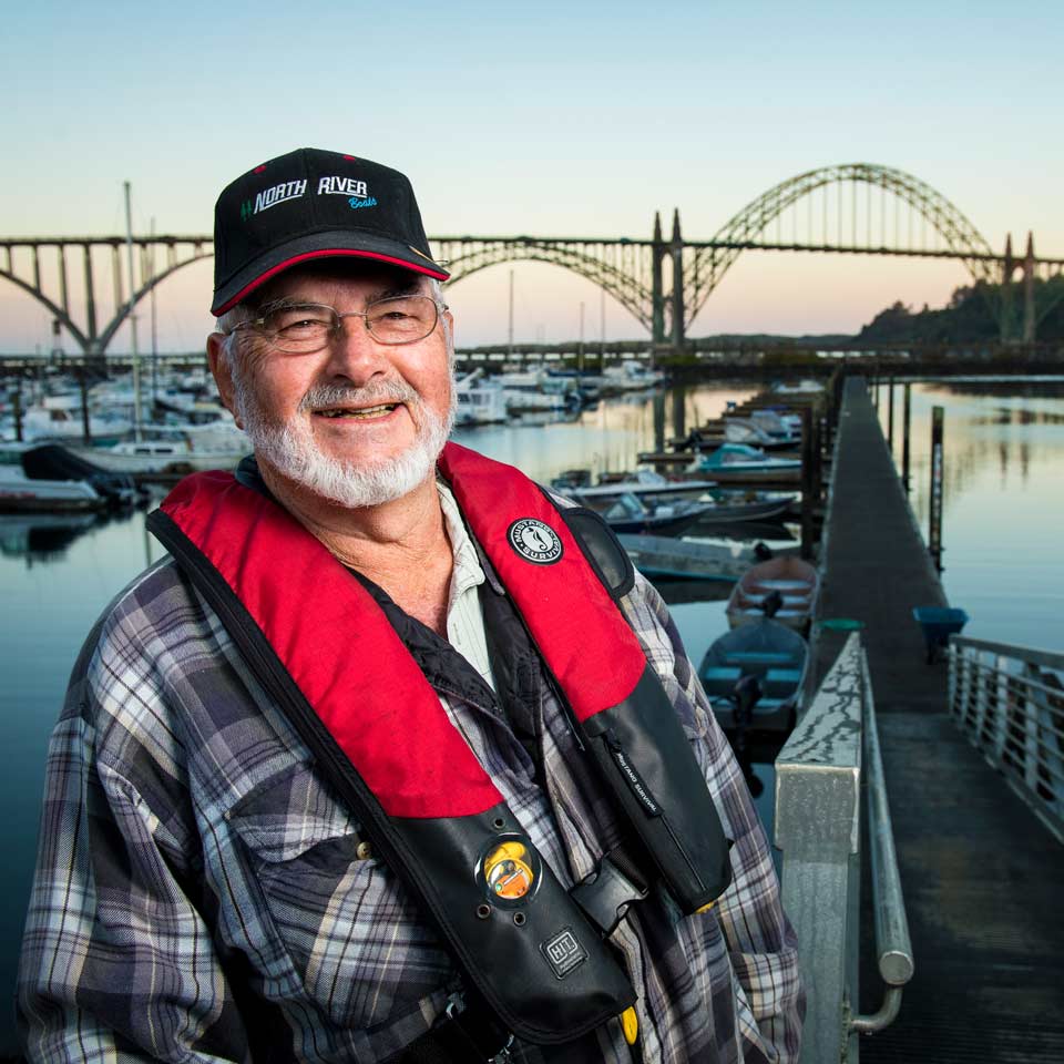 A smiling Roger on the dock at Yaquina bay. He's wearing a bright red life vest.