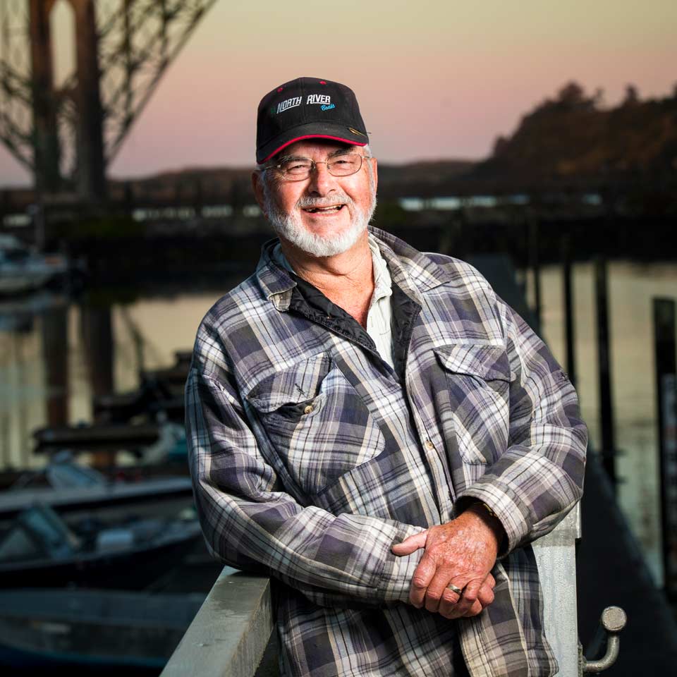 Roger Seals laughs as he leans back on a dock rail with the sky glowing in the colors of a sunrise.