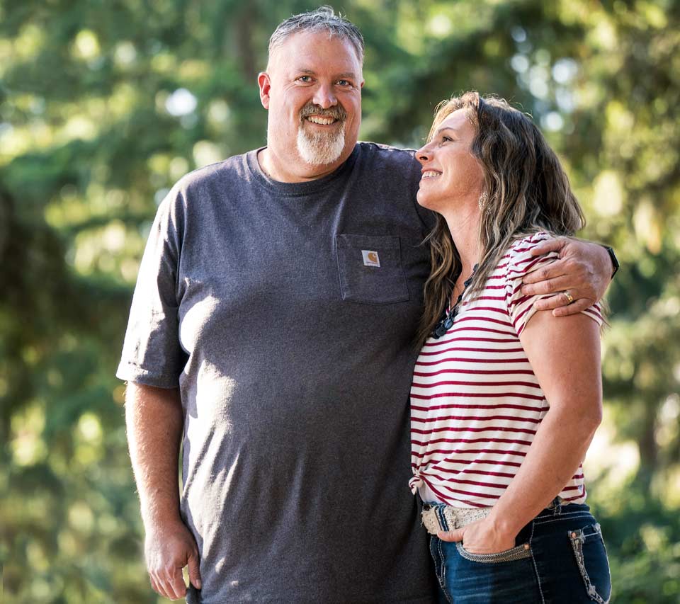Angie looks up to Scott. Both are smiling and standing outdoors on a beautiful day.