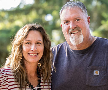 Scott and his wife smiling while standing outdoors on a beautiful day.