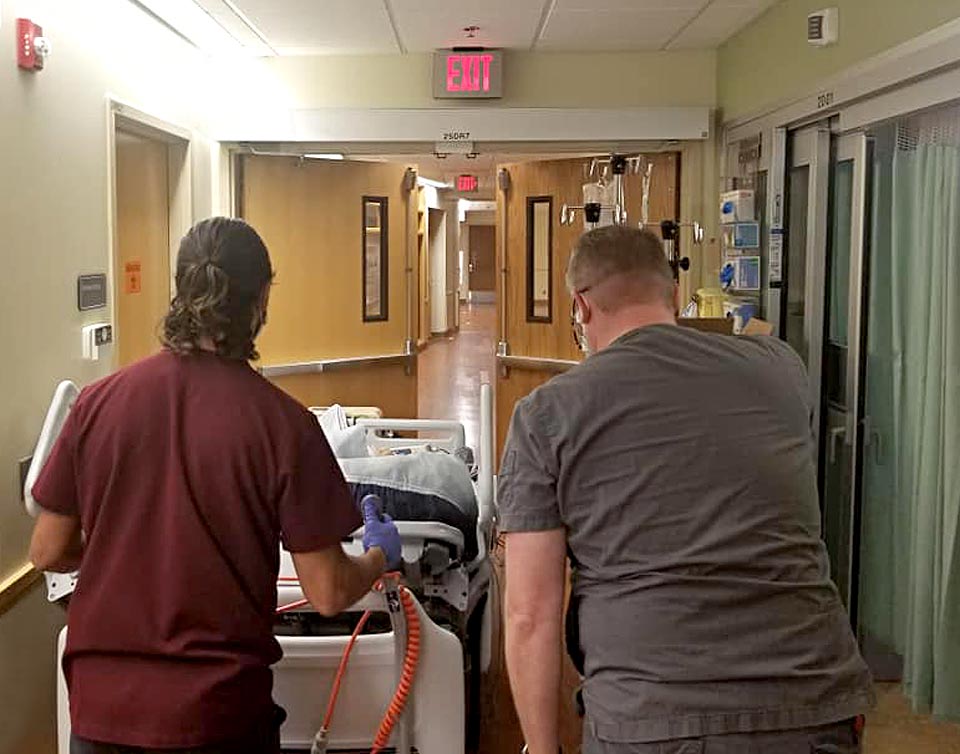 Scott being wheeled down the hall in his hospital bed.