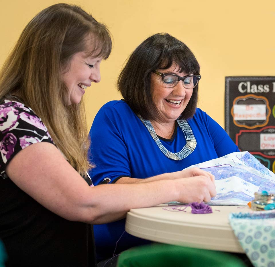 Vallie and volunteer smiling as the quilt together.