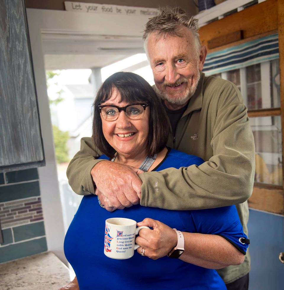 Lynn embraces Vallie from behind as they stand in their cozy kitchen.