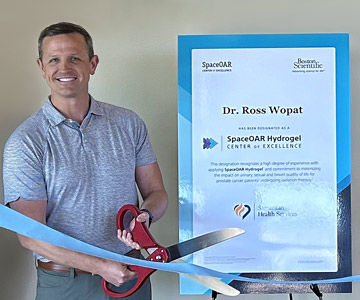 Dr. Ross Wopat holding an extra large pair of scissors in hands and cutting a blue ribbon.