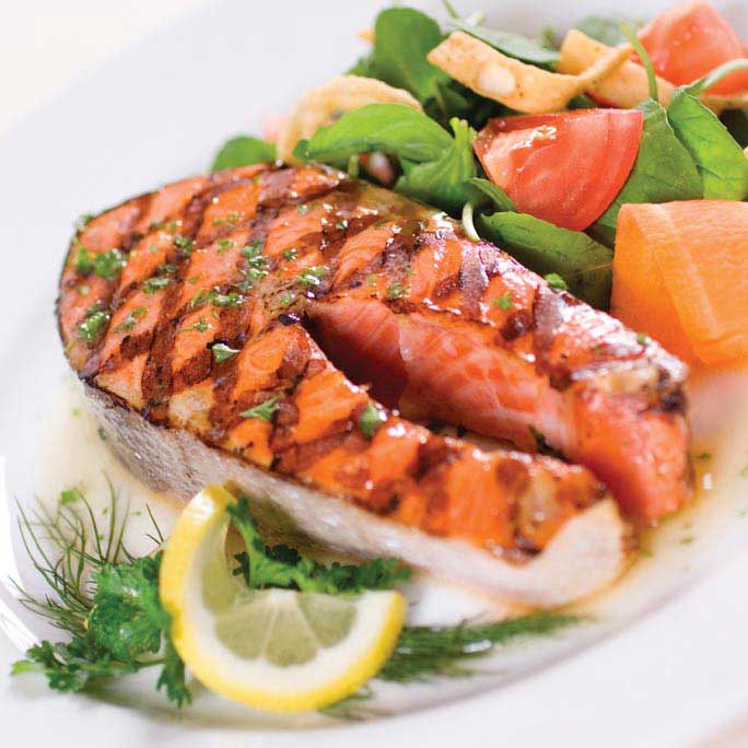 Plate of salmon with a lemon slice and a side of vegetables.
