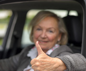 senior woman sitting in car with thumbs up sign