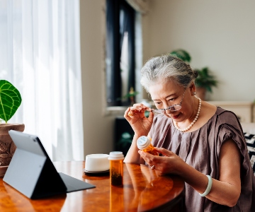 Senior woman looking at her prescription drug at the kitchen table with a computer.