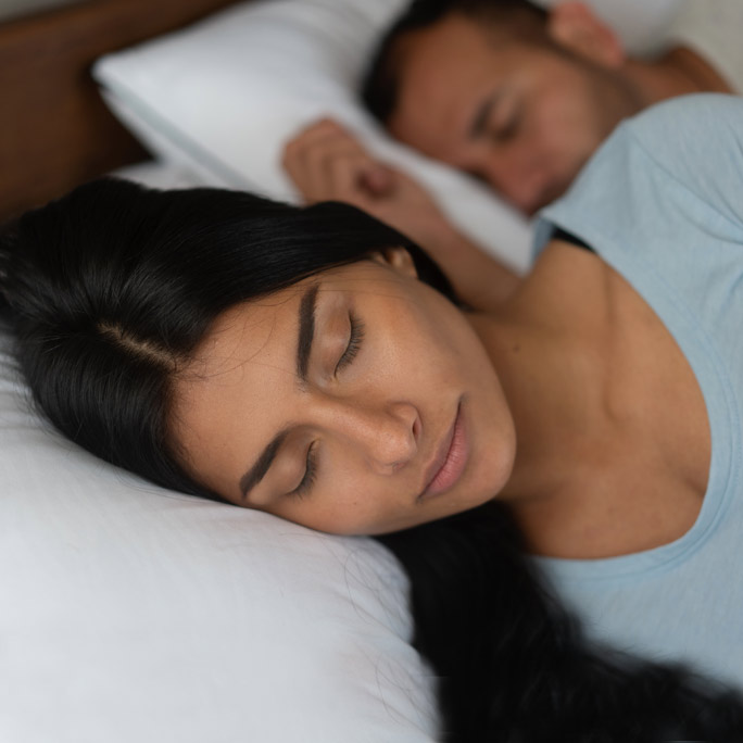 Sleeping woman in blue shirt, with her partner behind her.