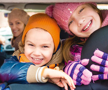 Two young sisters looking out the back window of their car smiling and dressed for cold weather.
