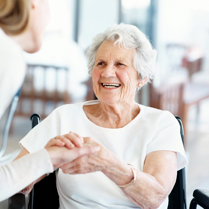 Elderly white woman in a wheel chair holding someone's hand.
