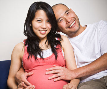 Smiling pregnant person with their partner holding their belly.