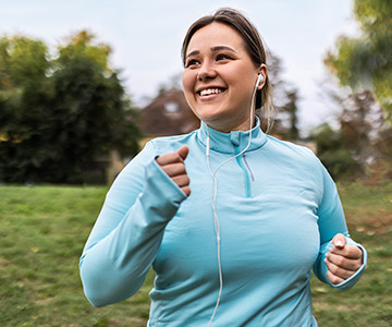 A woman smiling as she jogs through the park. Weight loss surgery article.