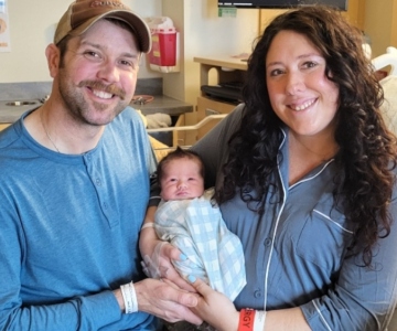 Man and woman smile while holding a newborn baby between them.