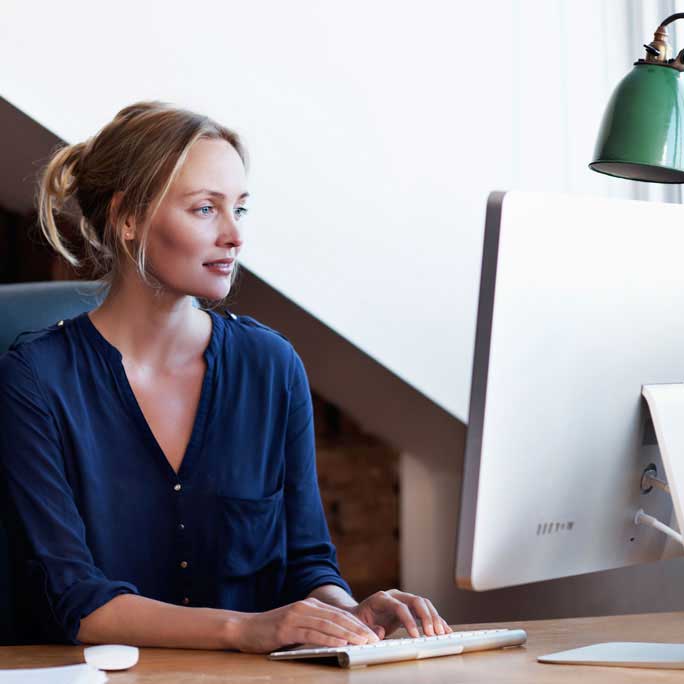 Woman sitting at a desk typing on her computer keyboard.