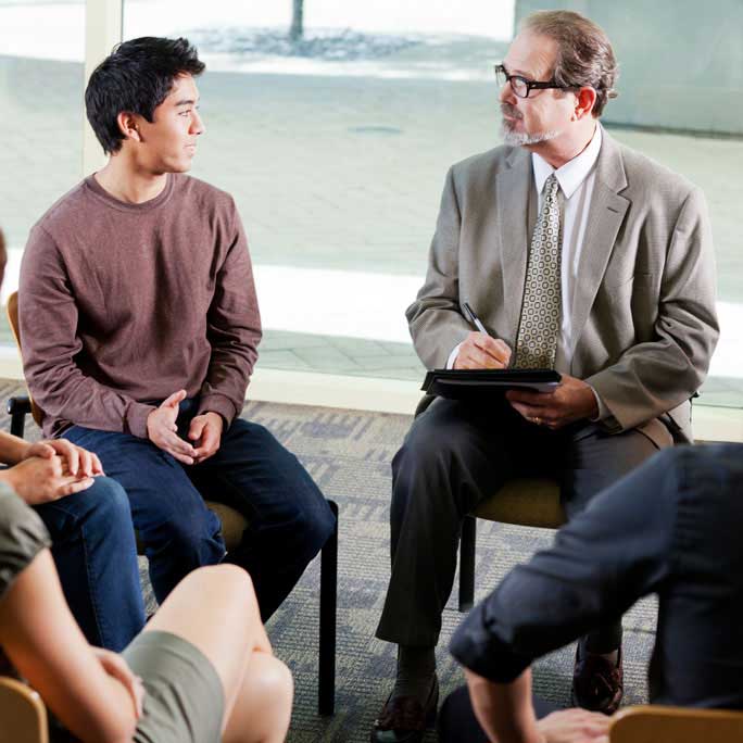 Group in chairs talk to person with clipboard.