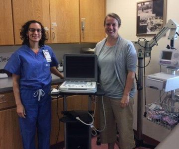 Two women in clinical scrubs pose with medical equipment