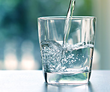 Water can help you keep your cool. A glass with water being poured in front of a cool blue-green background.