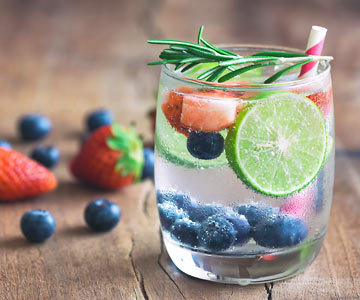 A glass of water with blueberries, strawberries, lime and rosemary.