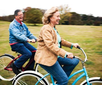 Older couple riding bikes by grassy field