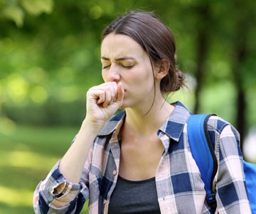 A student walking across campus coughs into her hand.