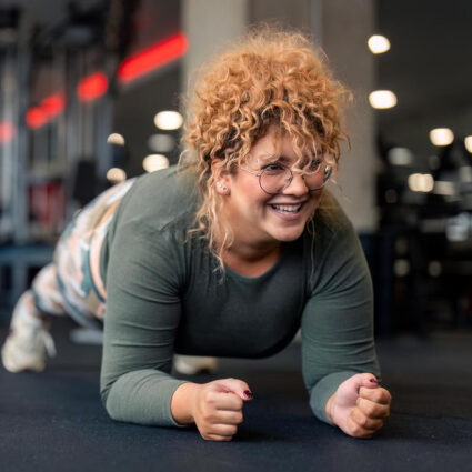 Smiling woman in a gym doing a plank.