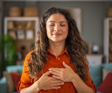 Woman practicing gratitude by placing her hands over her chest, closing her eyes and reflecting.
