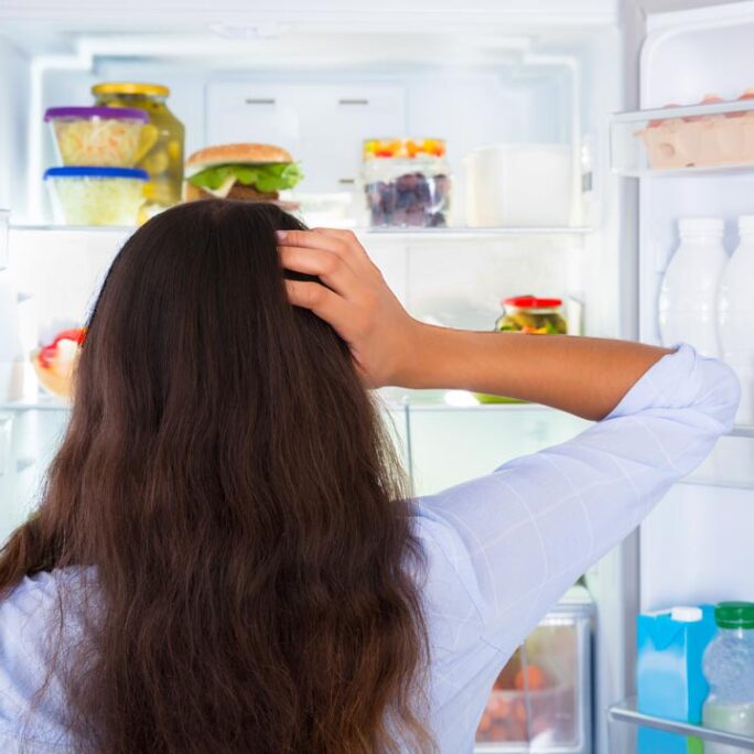 A woman standing in front of her fridge pondering what she was going to retrieve.