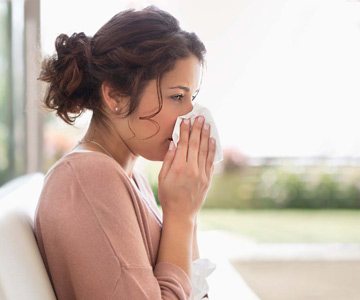 Woman sneezes into a tissue