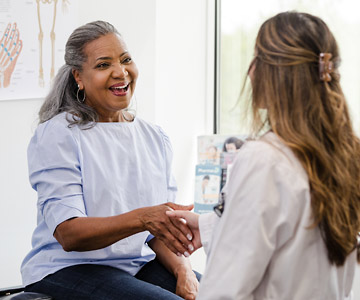 A woman talks with her doctor while sitting in an exam room.