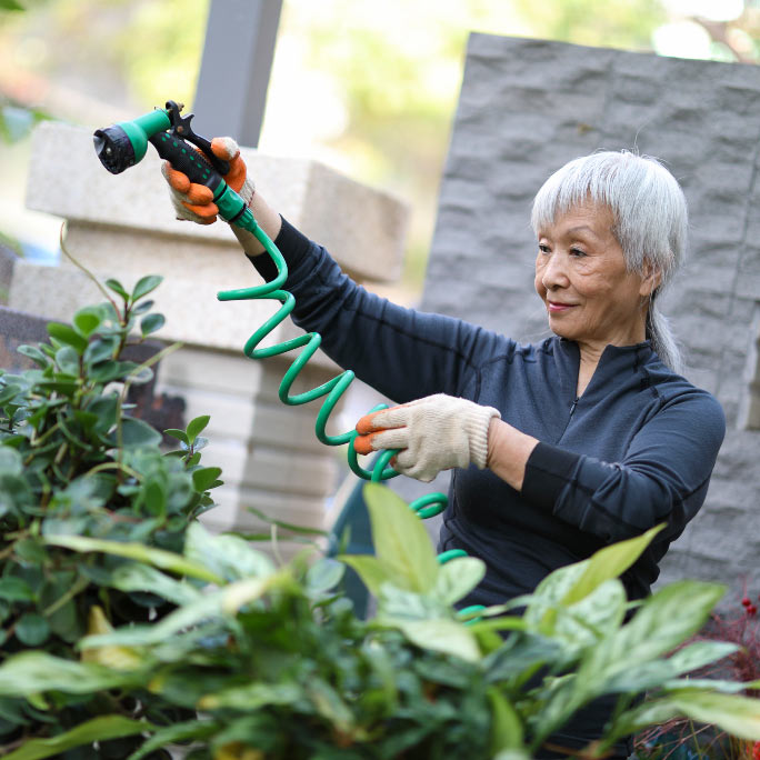Older woman watering her leafy garden.