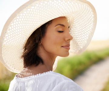 Woman wearing a wide brim hat while standing outside in the sunshine.