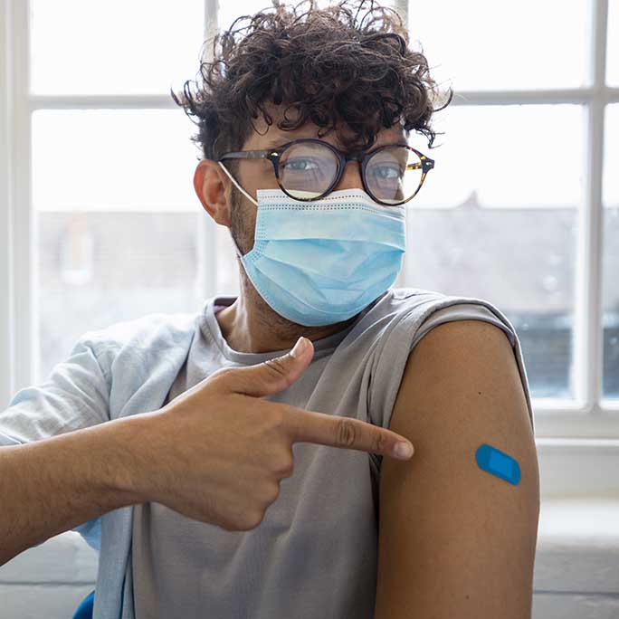 Young masked man points to band aid on arm